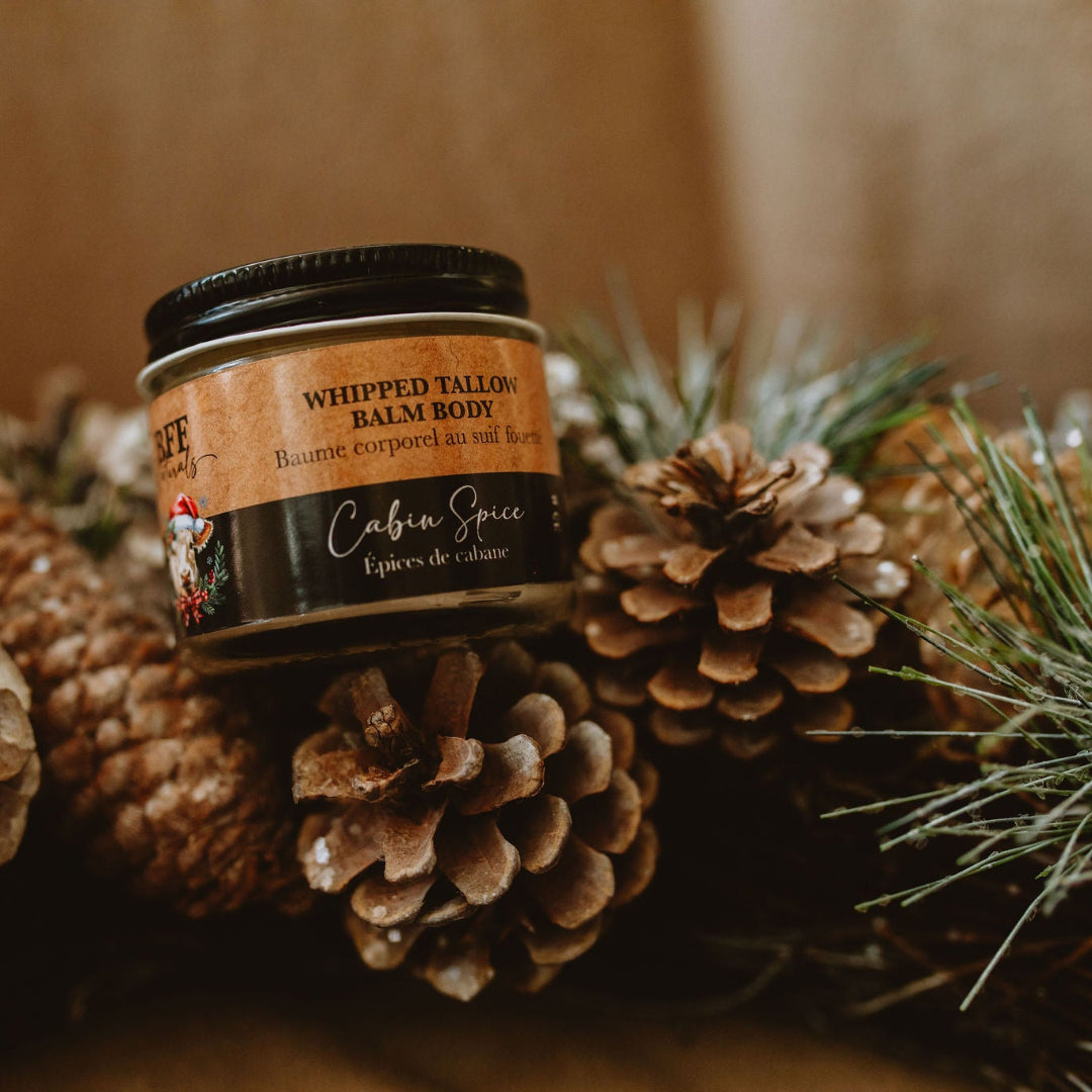 Jar of whipped balm surrounded by pinecones and evergreen branches on a blurred background