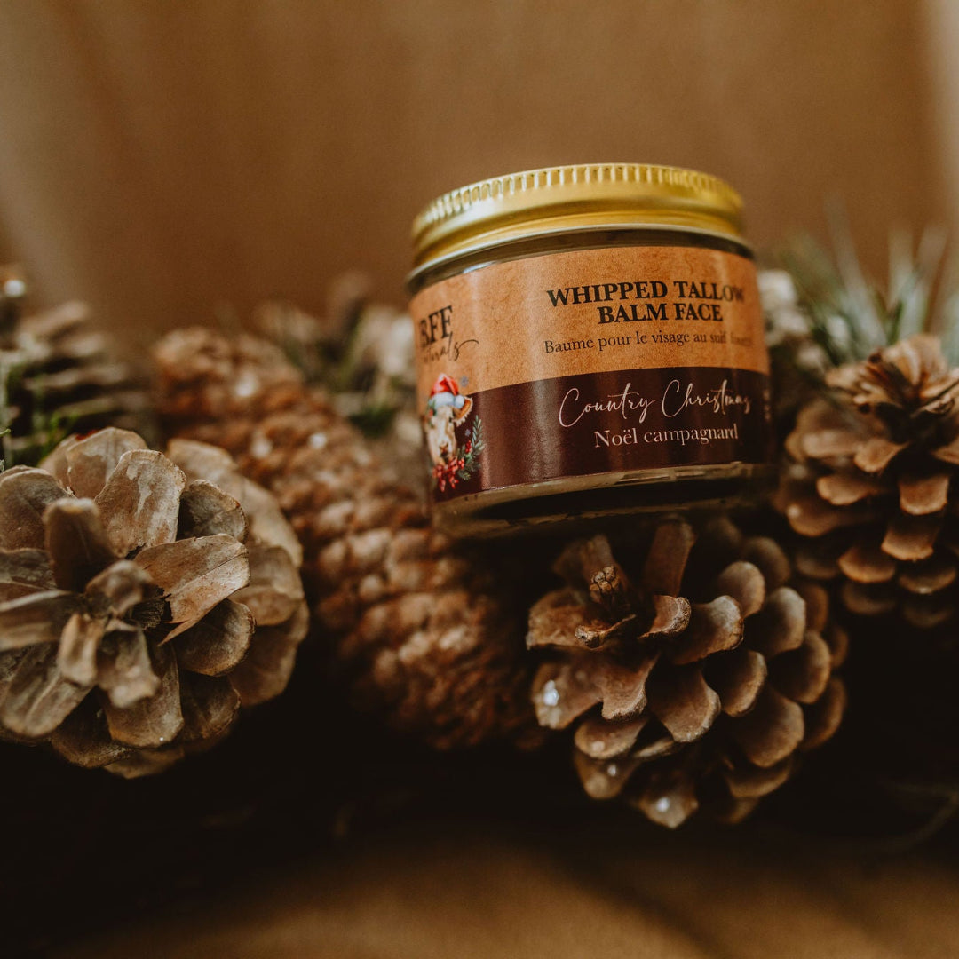 Jar of whipped tallow balm surrounded by pine cones and branches on a wooden surface
