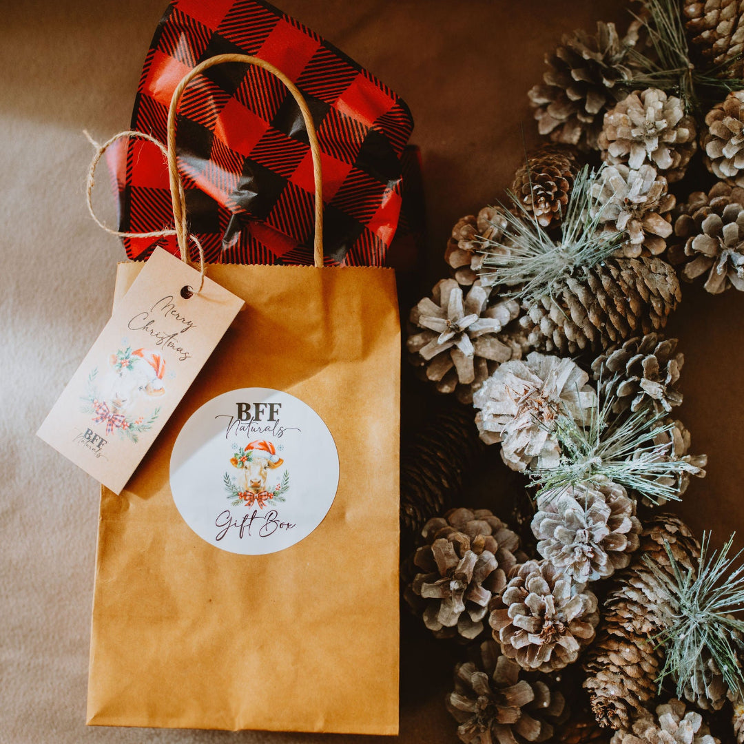 Gift bag with decorative tag next to a wreath made of pine cones and branches on a brown background